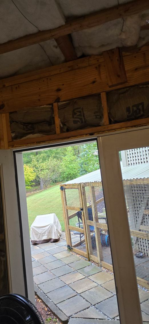 View from inside a structure with an open door to an outdoor patio with a covered object and a chicken coop.