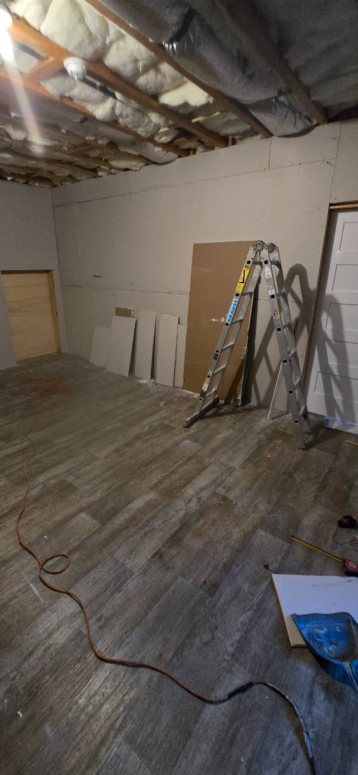 Room interior with wood-look flooring, ladder, and construction materials. Exposed ceiling beams and insulation.