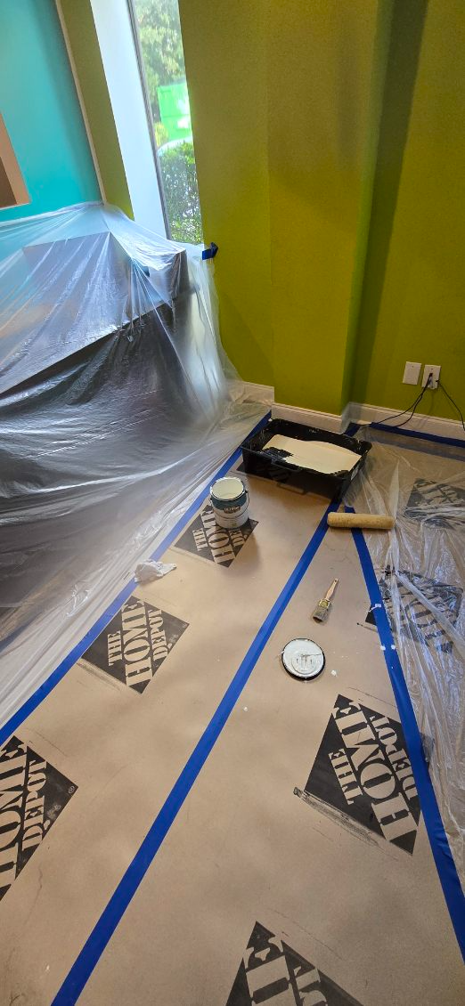 Room prepared for painting; drop cloths and tape on floor, paint supplies visible.