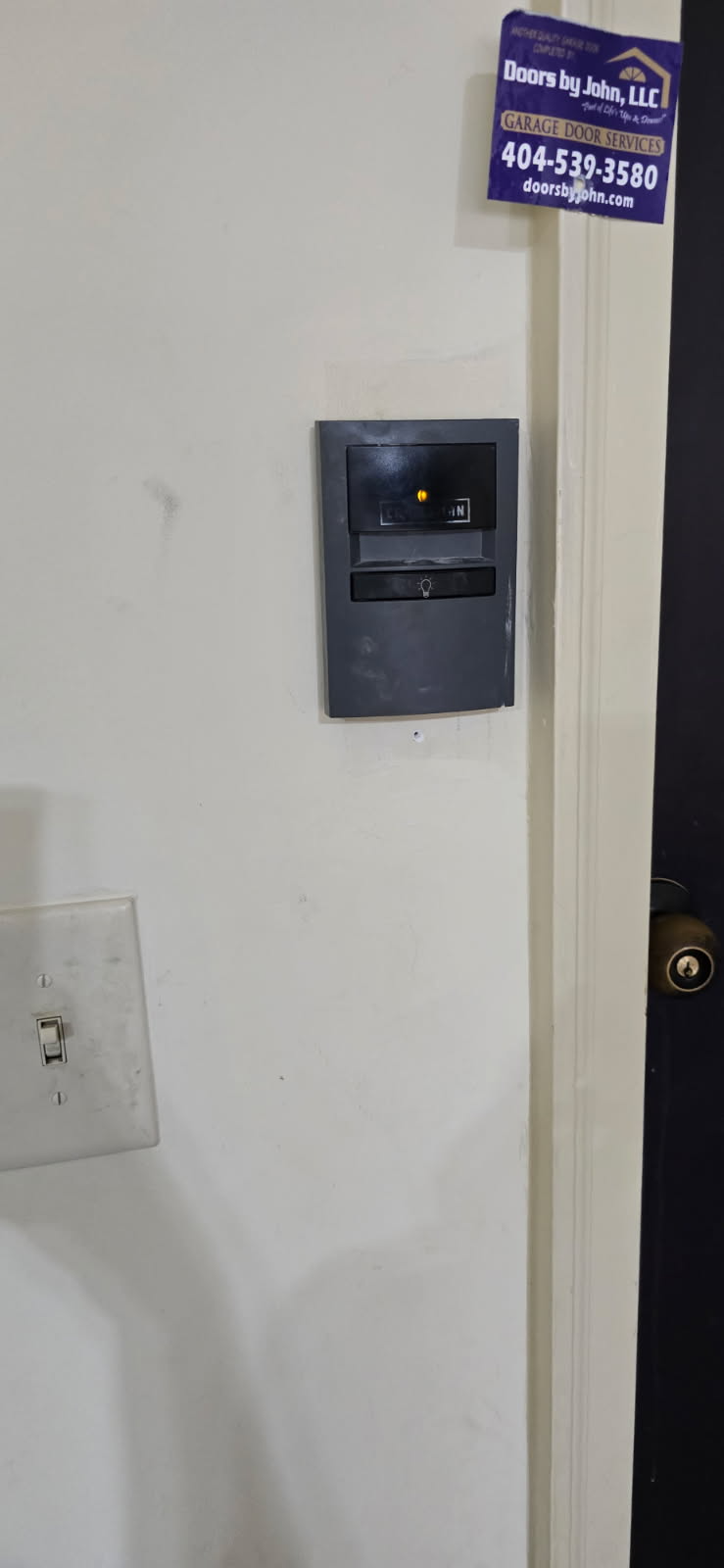 A security system keypad on a white door. A security sticker and a doorknob are also visible.