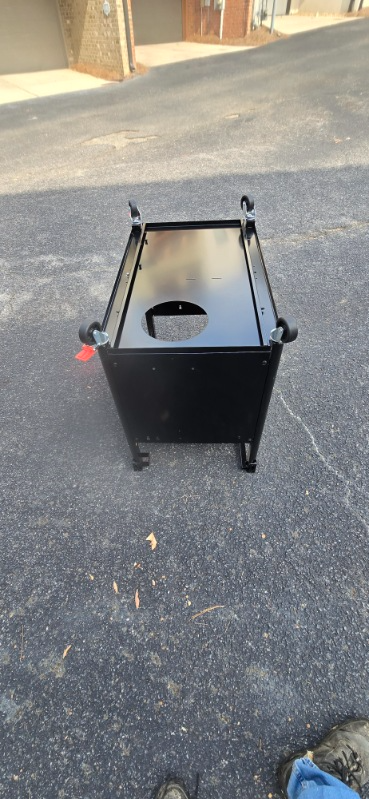 Black metal cart with a circular hole, on a paved surface.