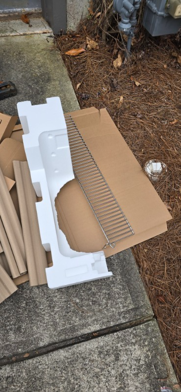 Cardboard packaging and styrofoam packing on a concrete surface, near some foliage.