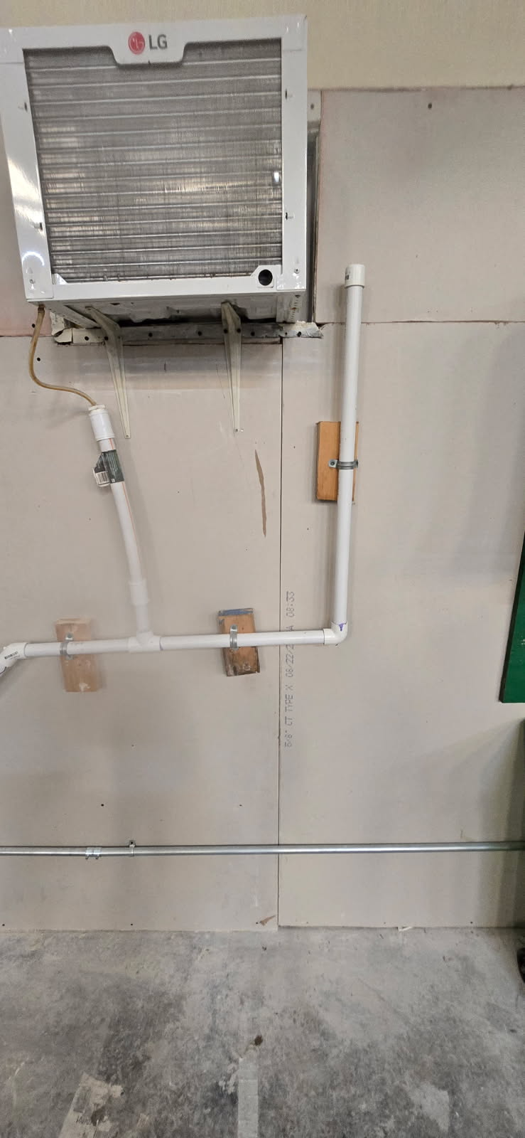 An LG air conditioner installed on a wall with PVC pipes below, above a concrete floor.