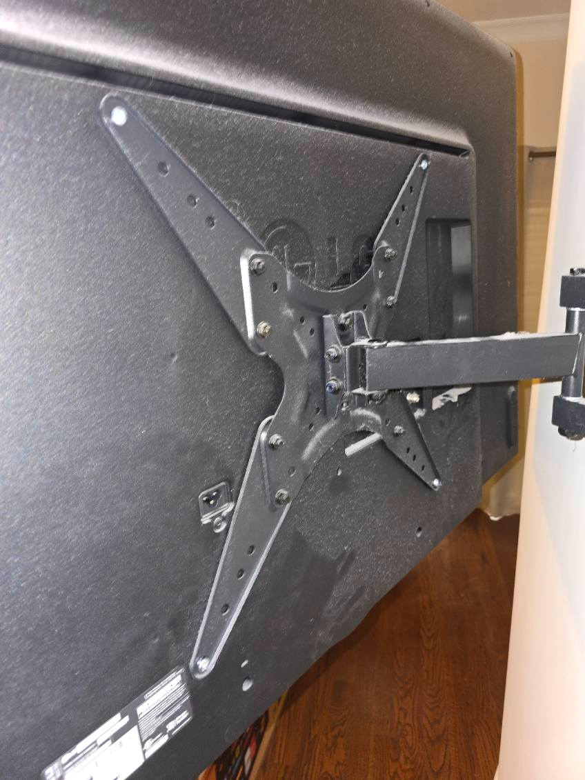Black TV mounted on a black wall bracket with a metal arm, attached to a wall.