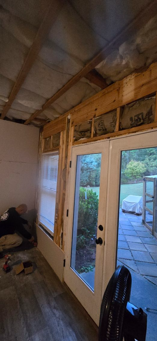 Interior of a room under construction with a door, window, and exposed wooden framing.