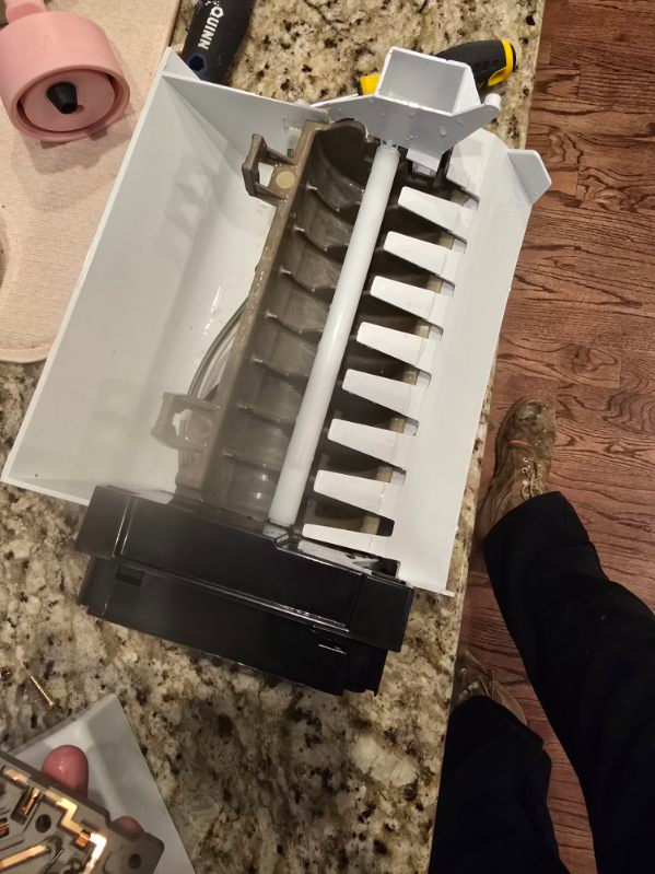 Opened white and black plastic appliance on a kitchen counter, showing internal gears and white paddle-like parts