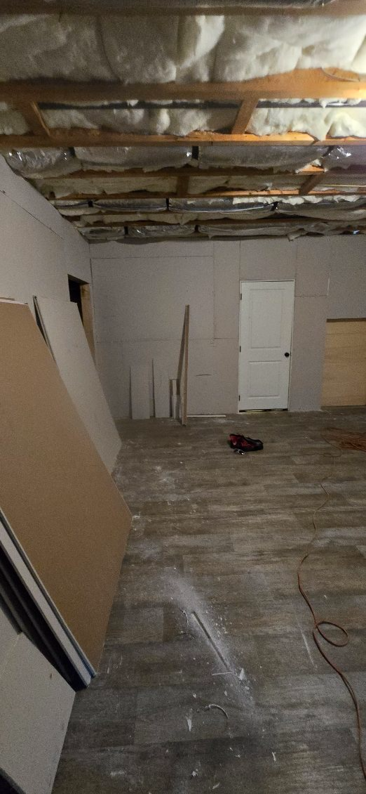 Unfinished basement room with exposed ceiling joists, insulation, and white walls and door