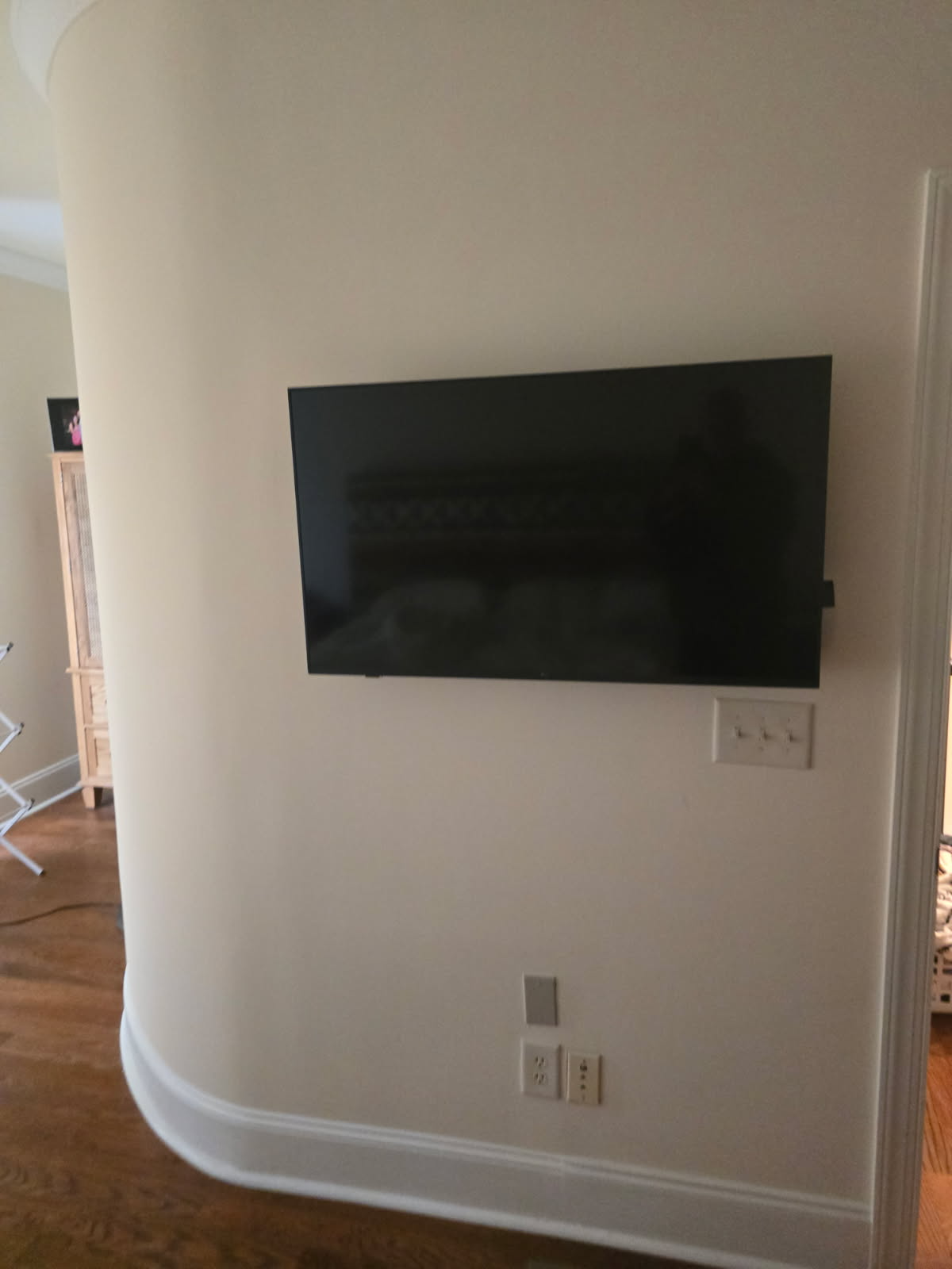 TV mounted on a curved, beige wall. Light switches and outlets are below the TV.