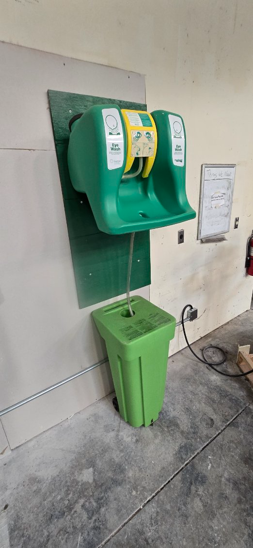 Green hand sanitizer dispenser with trash bin mounted on a wall in a tiled restroom area