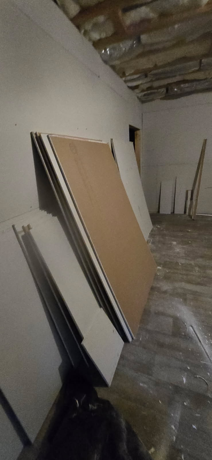 Stacks of drywall leaning against a wall in a room under construction.