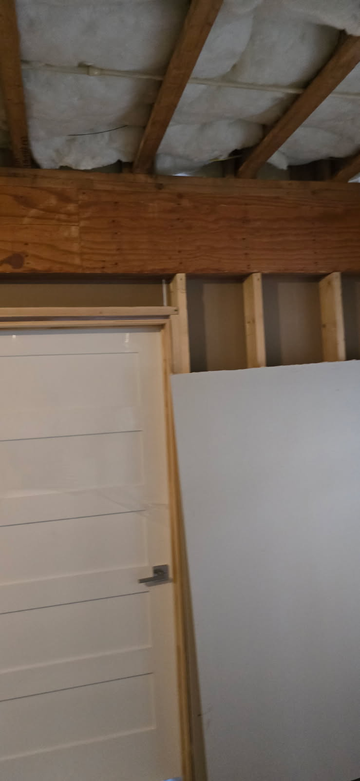 A partially constructed interior view with a door, drywall, and wooden beams visible.