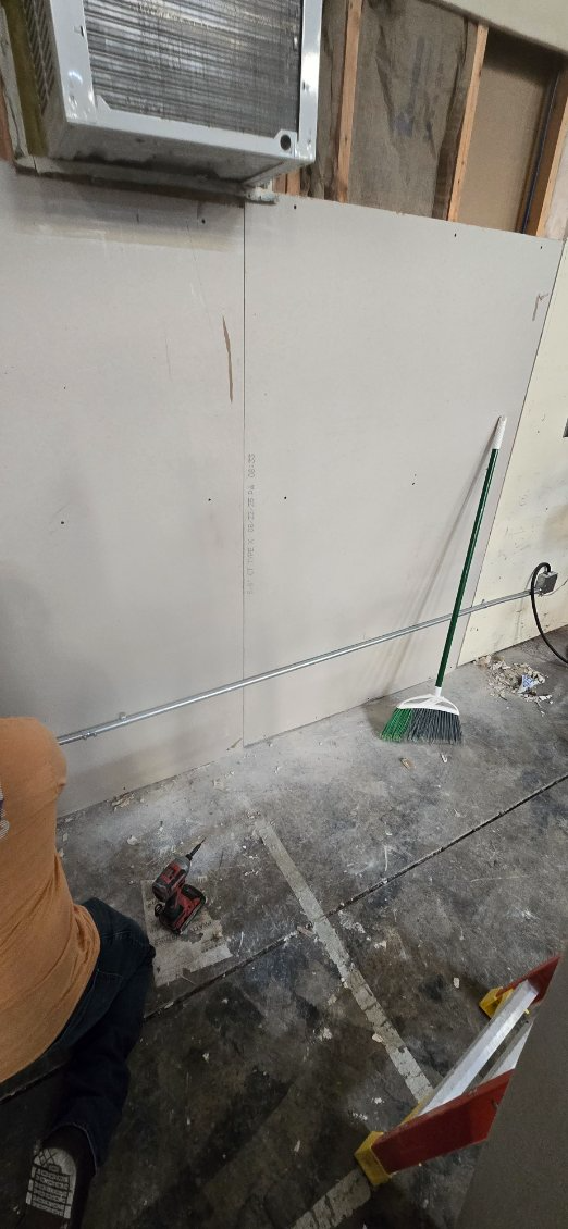 Chain strung across a room with drywall, a broom, and debris on the floor.