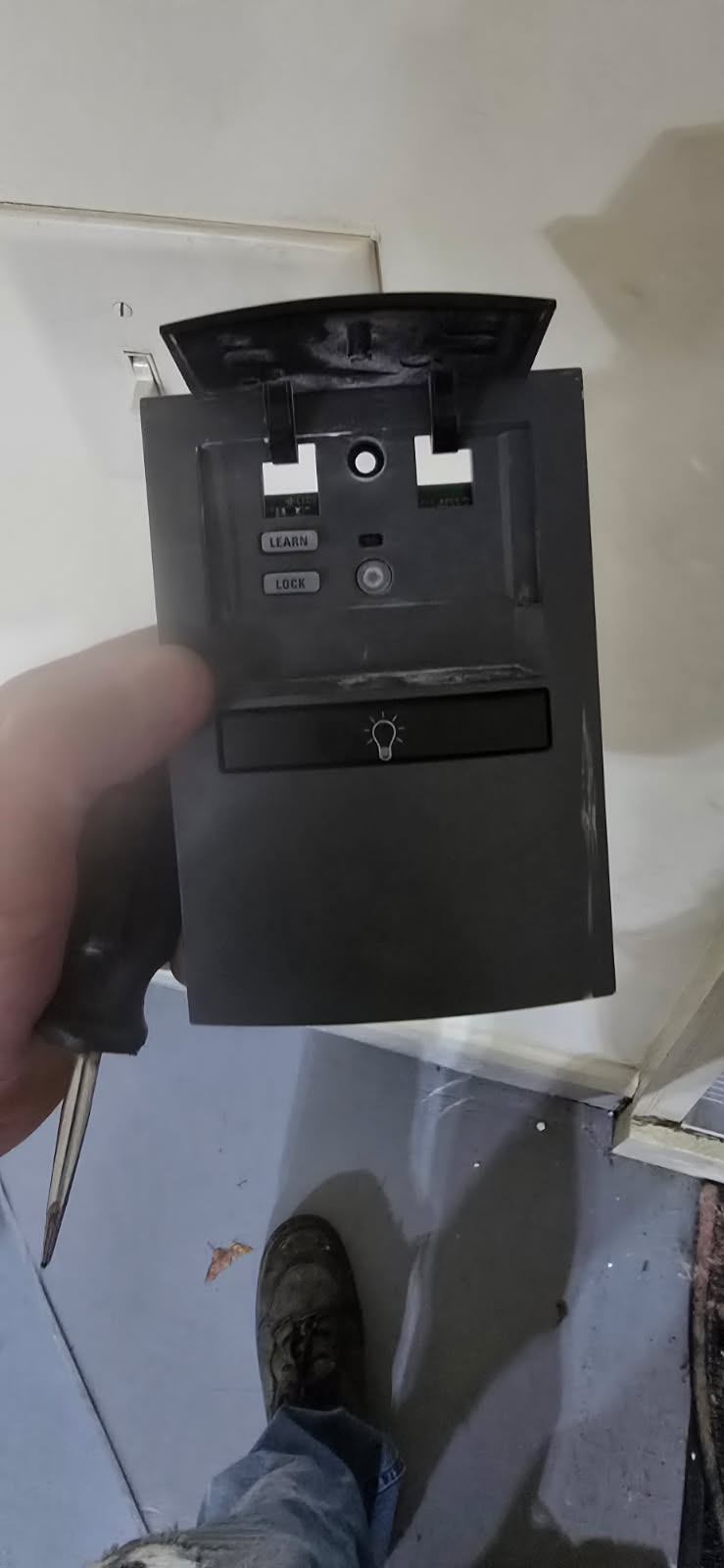 A person holding a dark gray computer case front panel. The panel has USB ports, and a drive bay.