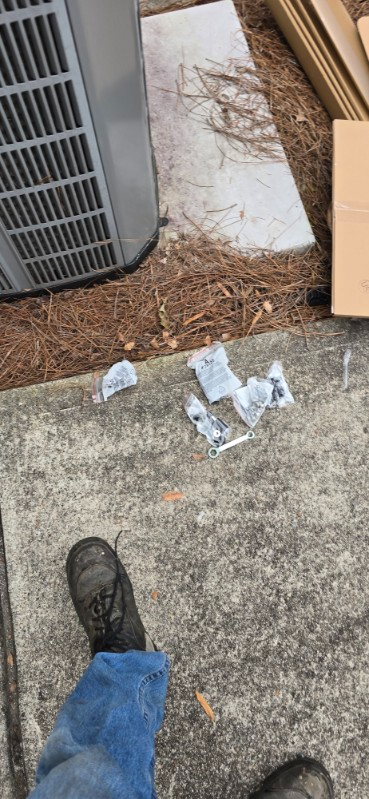 Person standing next to air conditioning unit. Trash on the concrete. Blue jeans and work boots.
