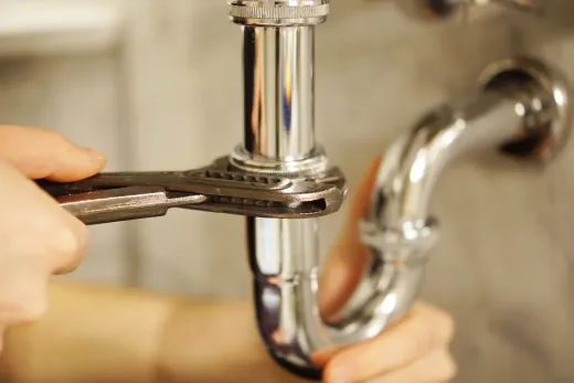 Hands tightening a chrome sink drain pipe with a wrench under a sink