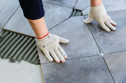 Gloved hands aligning gray paving stones on an outdoor patio.
