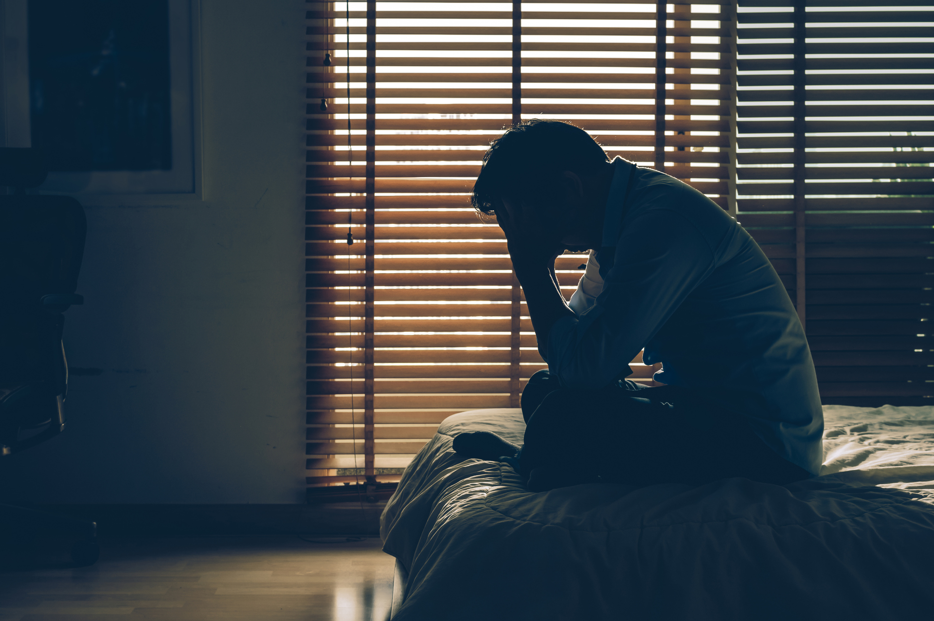 A man is sitting on a bed with his head in his hands.