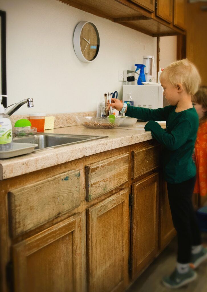 A young boy is washing dishes in a kitchen sink.