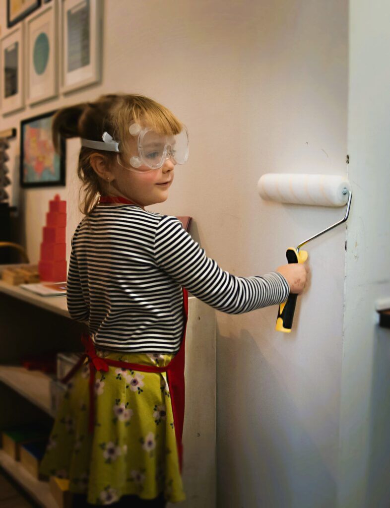 A little girl is painting a wall with a paint roller.
