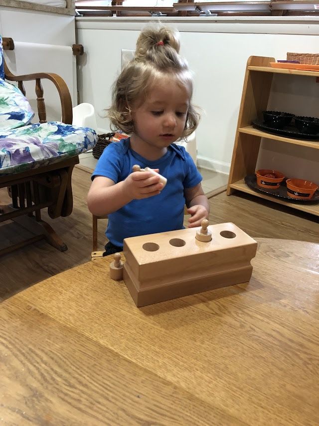 A little girl is sitting at a table playing with a wooden toy.
