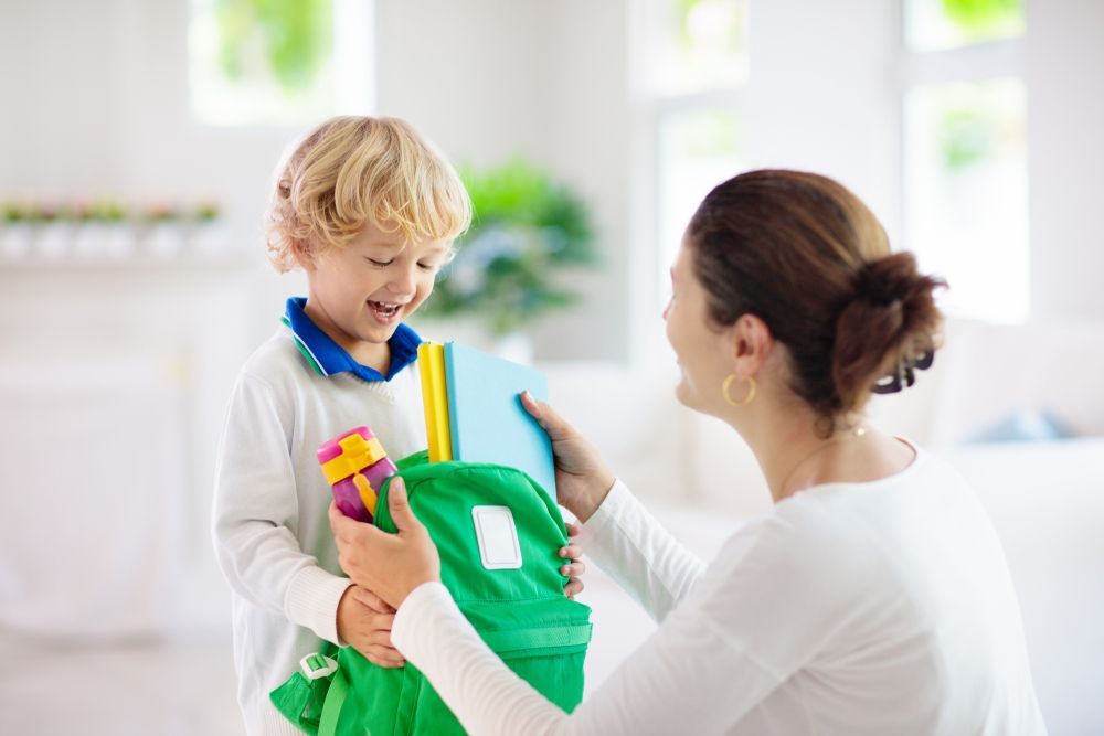 A woman is holding a green backpack and talking to a young boy.