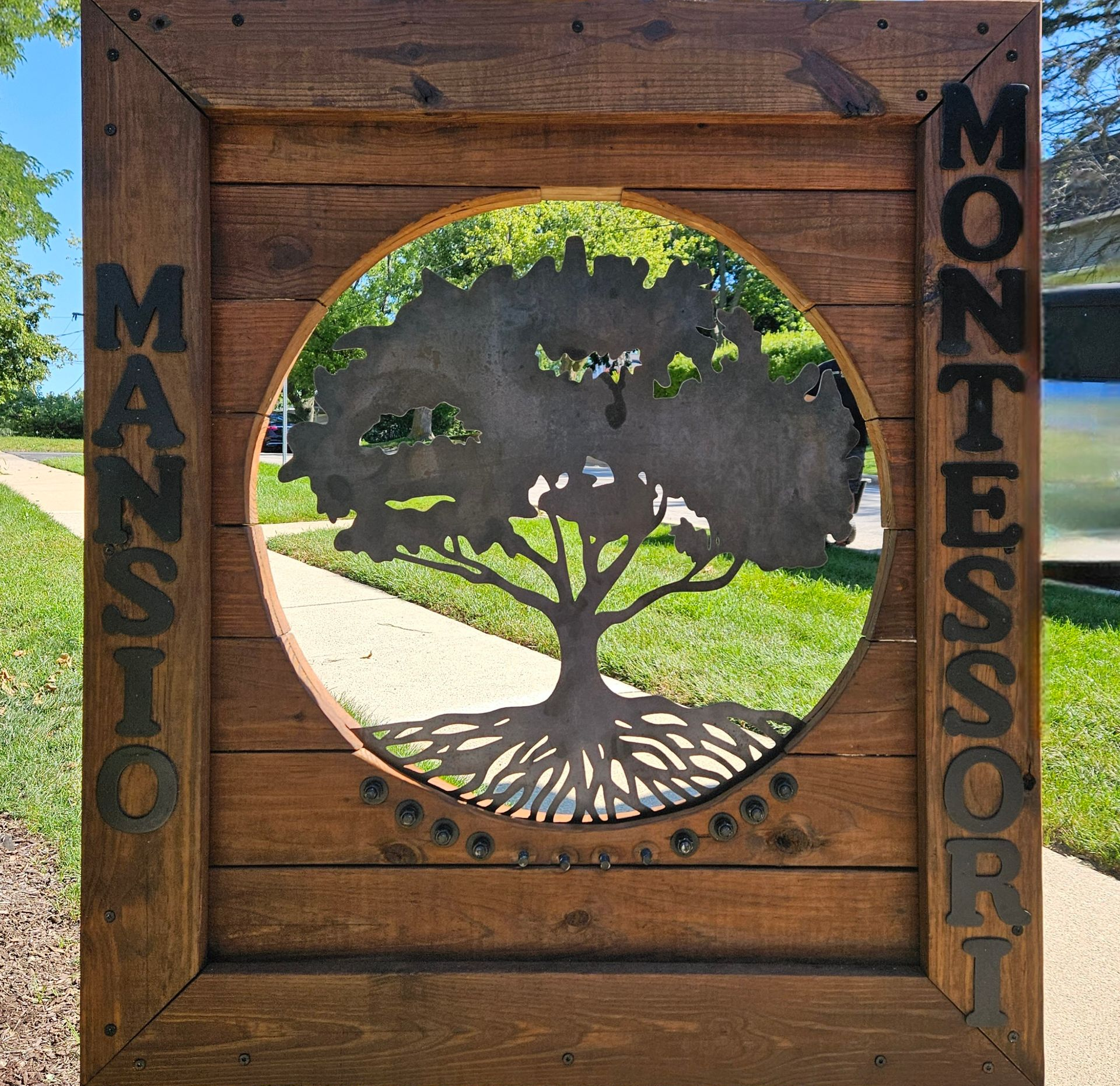 Wooden Masco Montessori sign with a cutout tree in a sunny outdoor setting