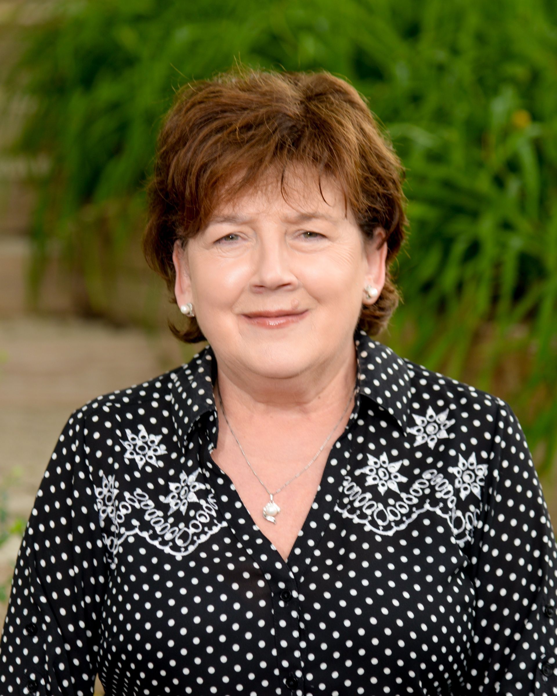 A woman wearing a black shirt and a necklace is smiling in a circle.