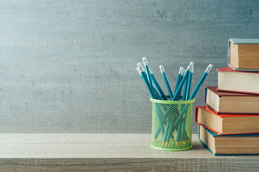 A pencil holder filled with pencils next to a stack of books on a table.