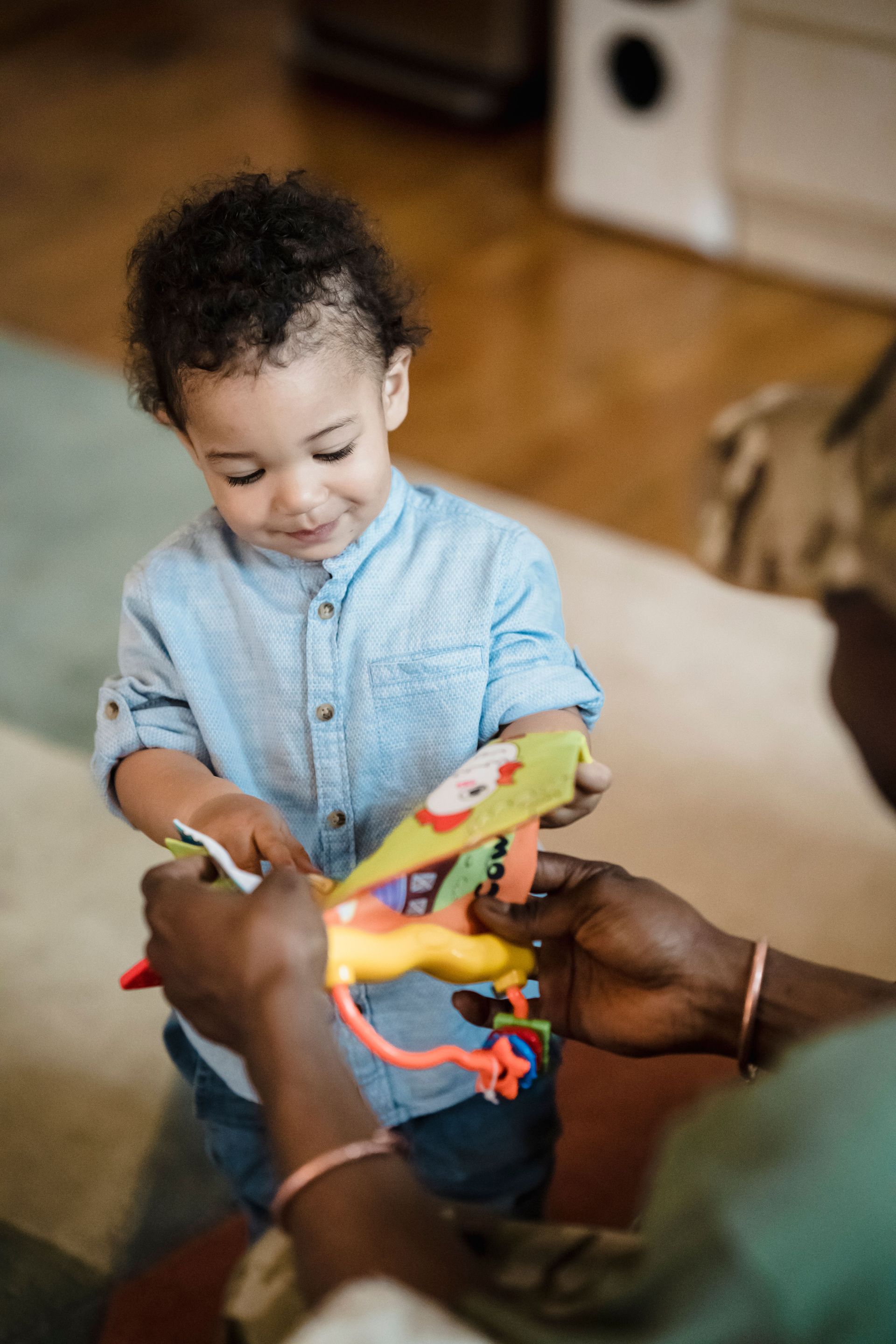 Adult hands holding a colorful toy for a child in a home setting