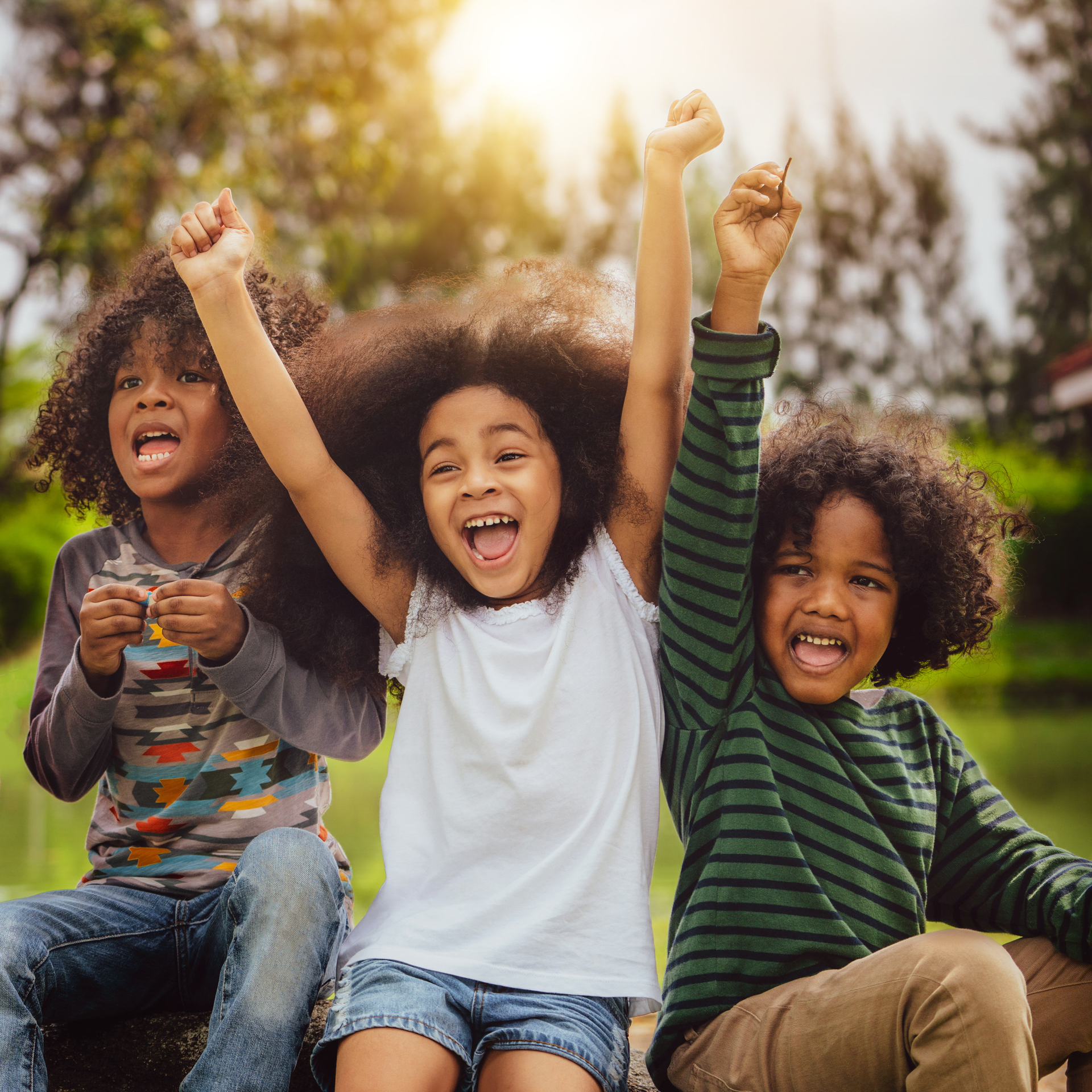 Three children are sitting on a rock with their arms in the air.