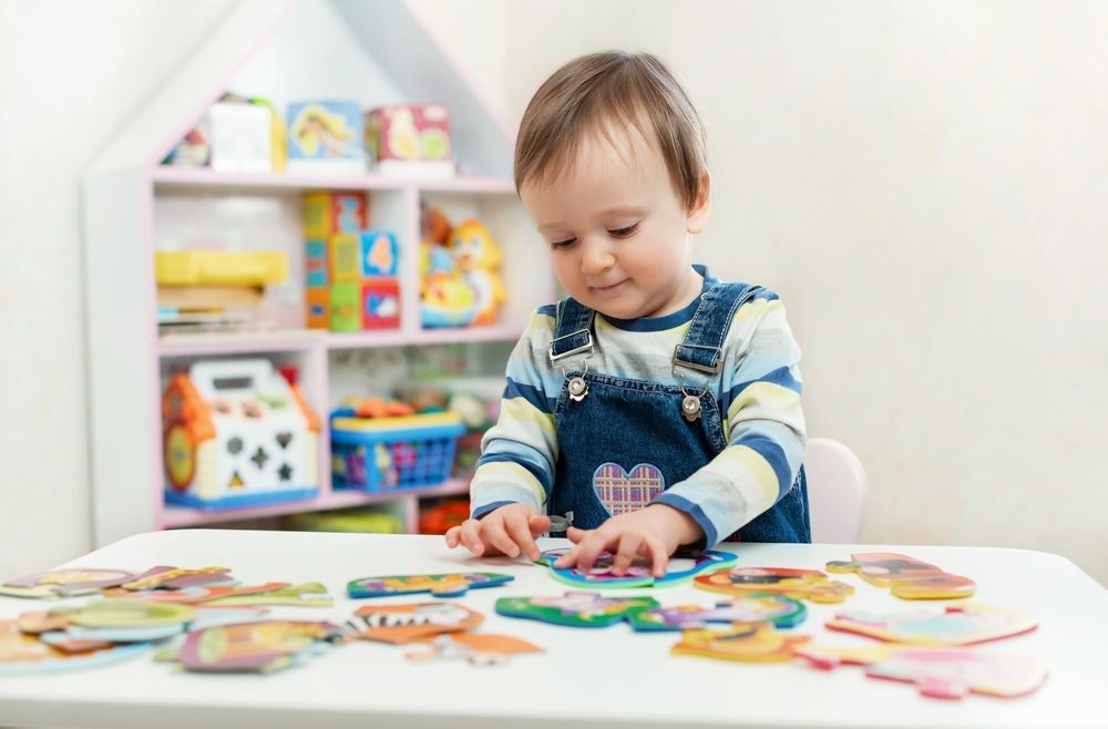 A toddler is sitting at a table playing with puzzles.