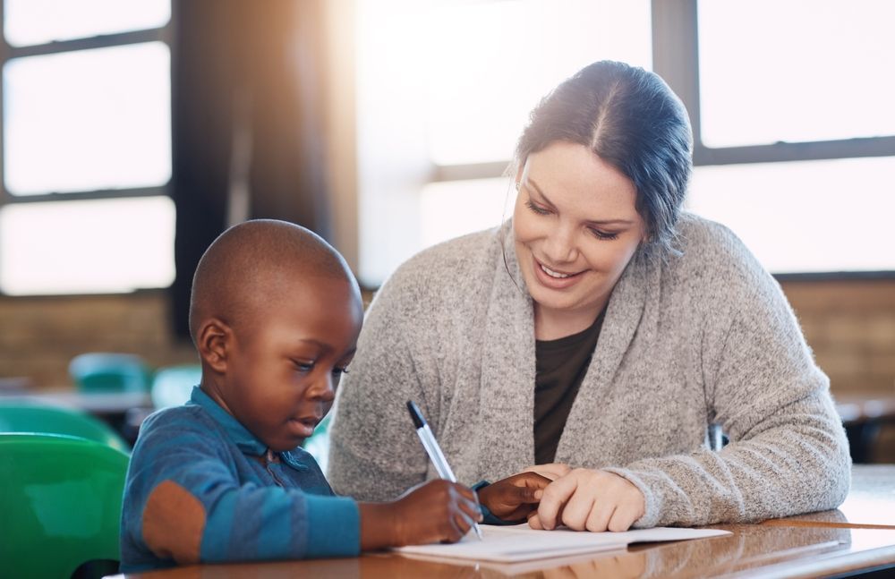 Montessori teacher guiding a young child with writing during hands-on classroom learning.