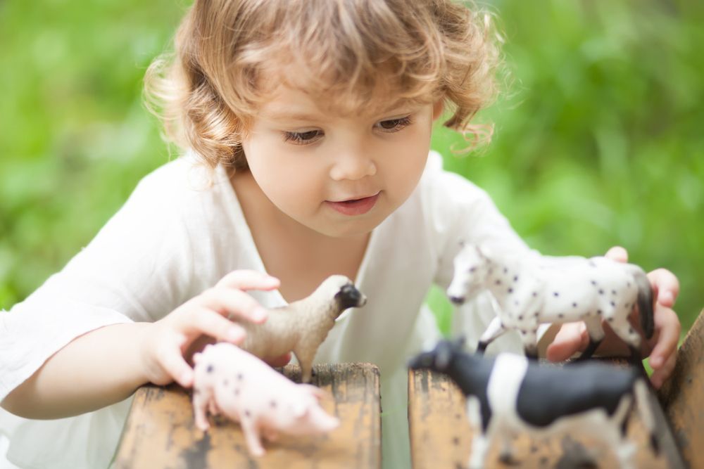 A little girl is playing with toy animals on a wooden table.
