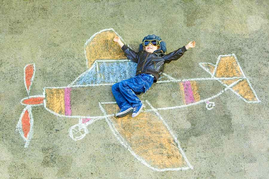 A child is laying on the ground in a chalk drawing of an airplane.