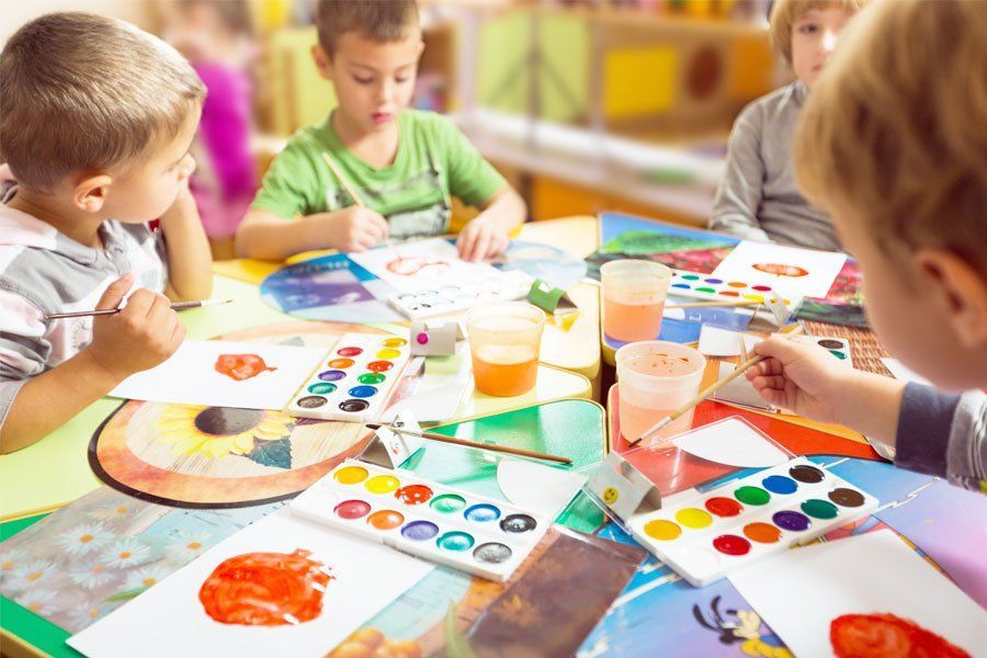 A group of children are sitting at a table painting with watercolors.