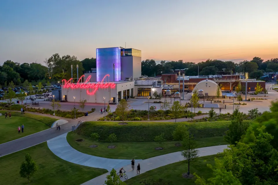 An aerial view of the illuminated Factory at Franklin complex at dusk, featuring a neon sign and surrounding green park.