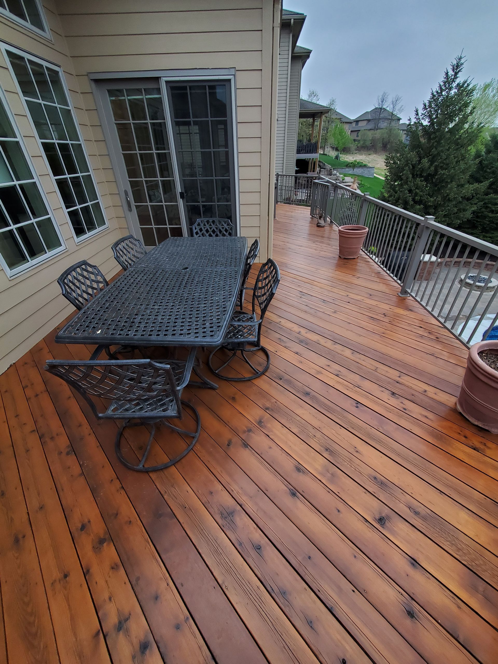 Wooden deck with wrought-iron table and chairs, adjacent to a house with a sliding glass door.
