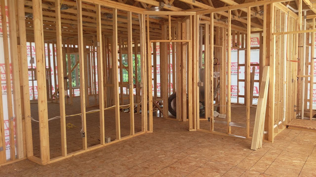 Interior view of a building under construction, showing wooden wall framing and a doorway.