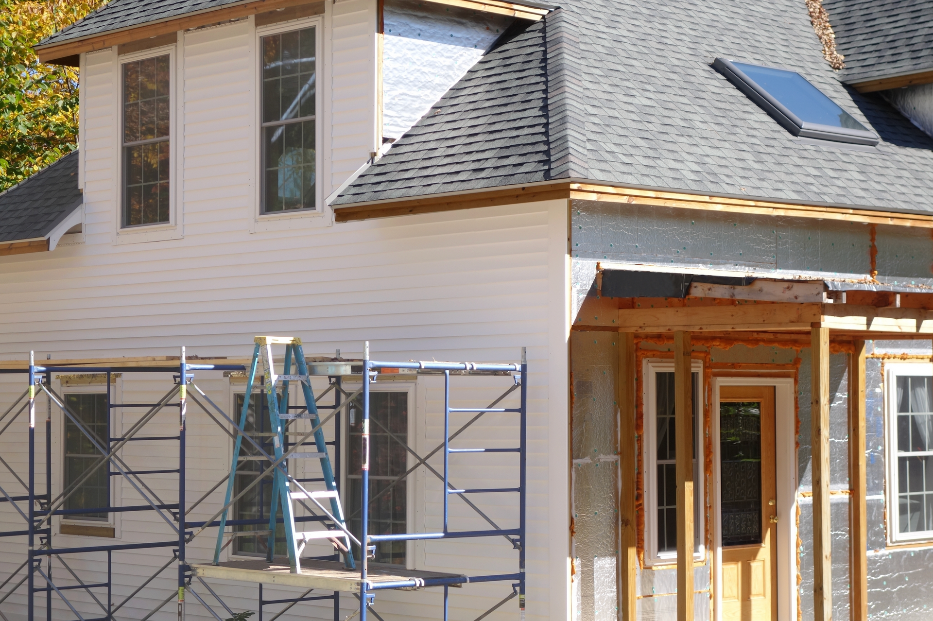 House under construction; one side finished with white siding, the other unfinished, showing insulation and framing.