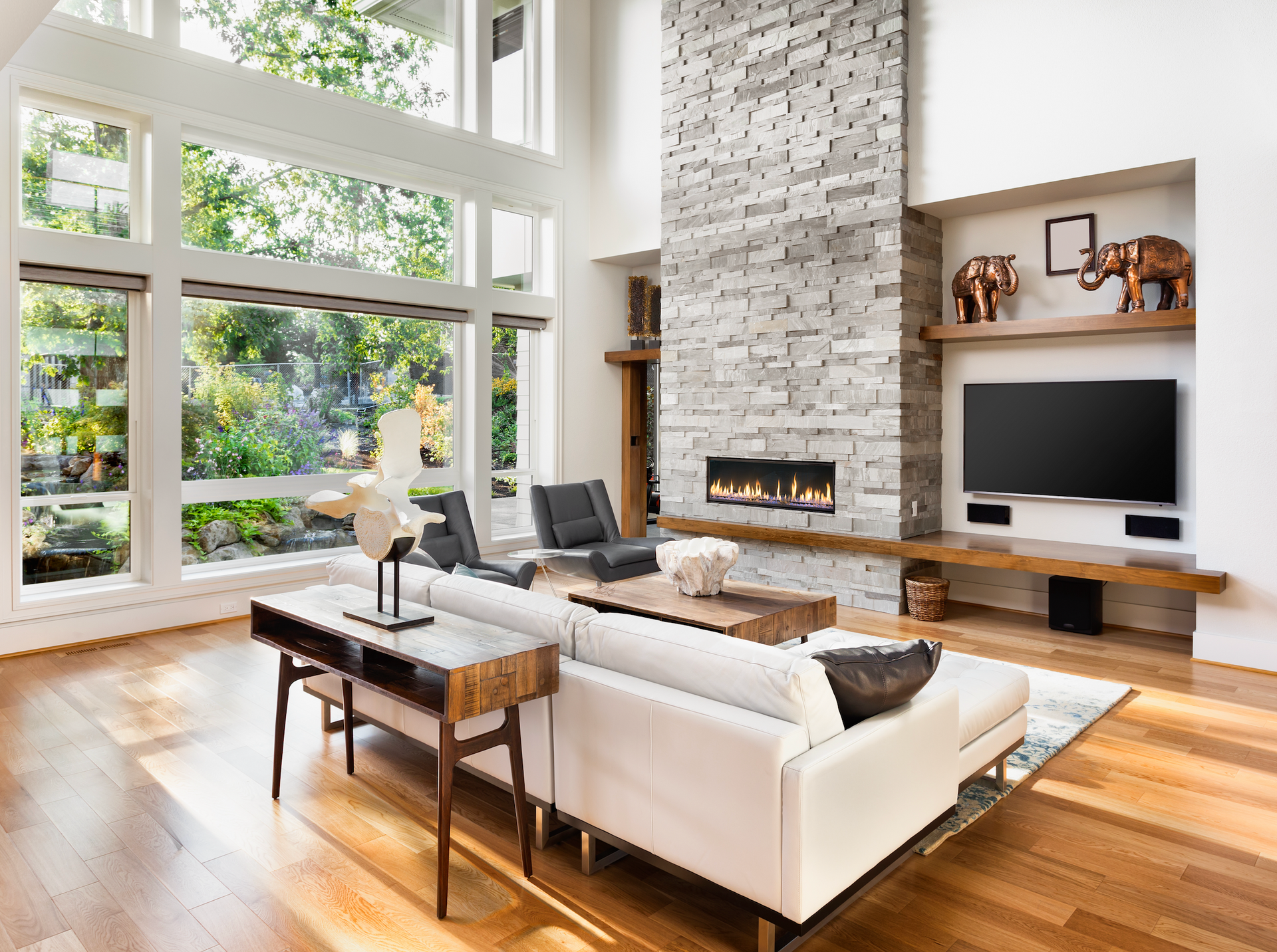 Living room with large windows, stone fireplace, white sofa, and wooden floors.