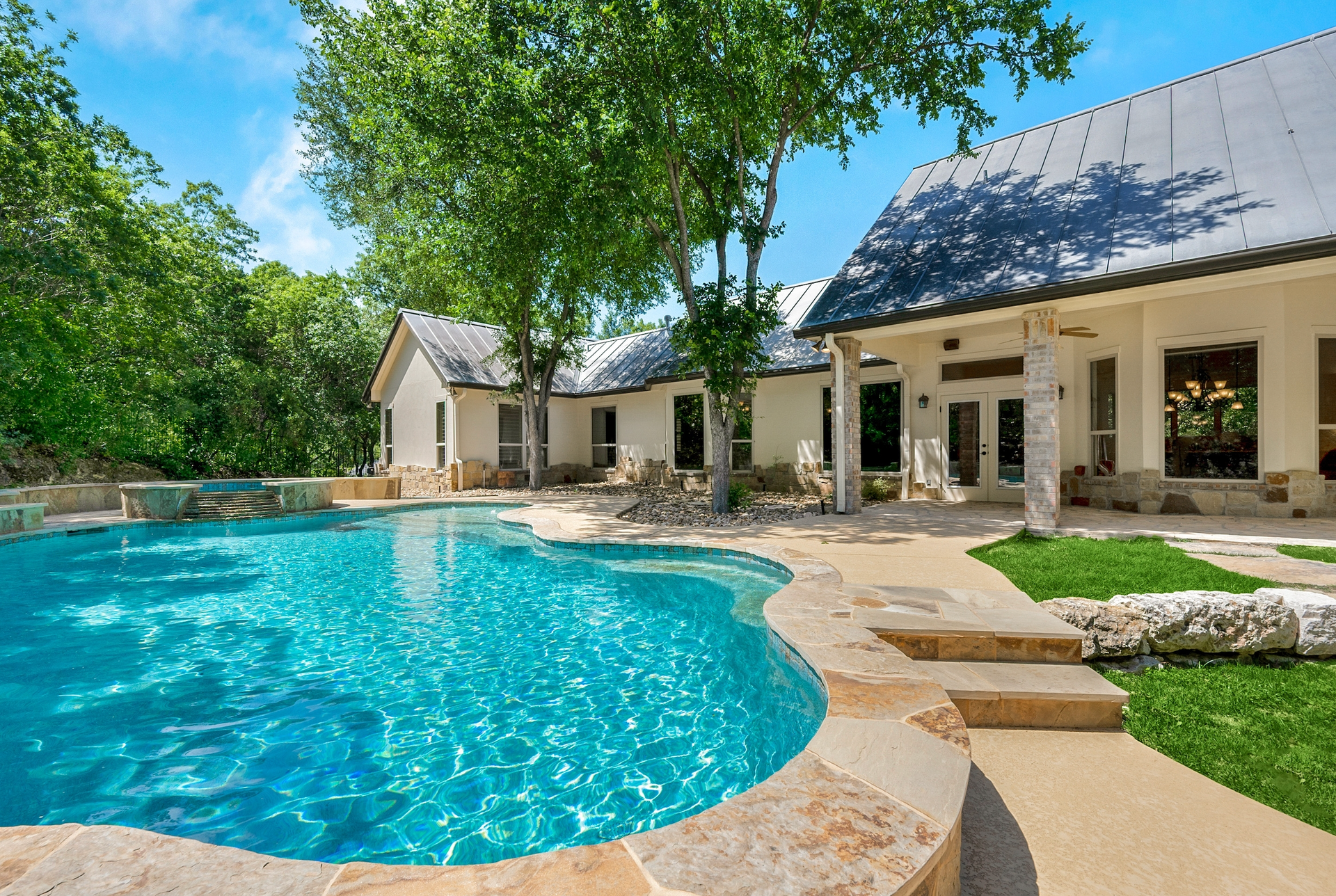 Pool in front of a white house with a metal roof, sunny day.