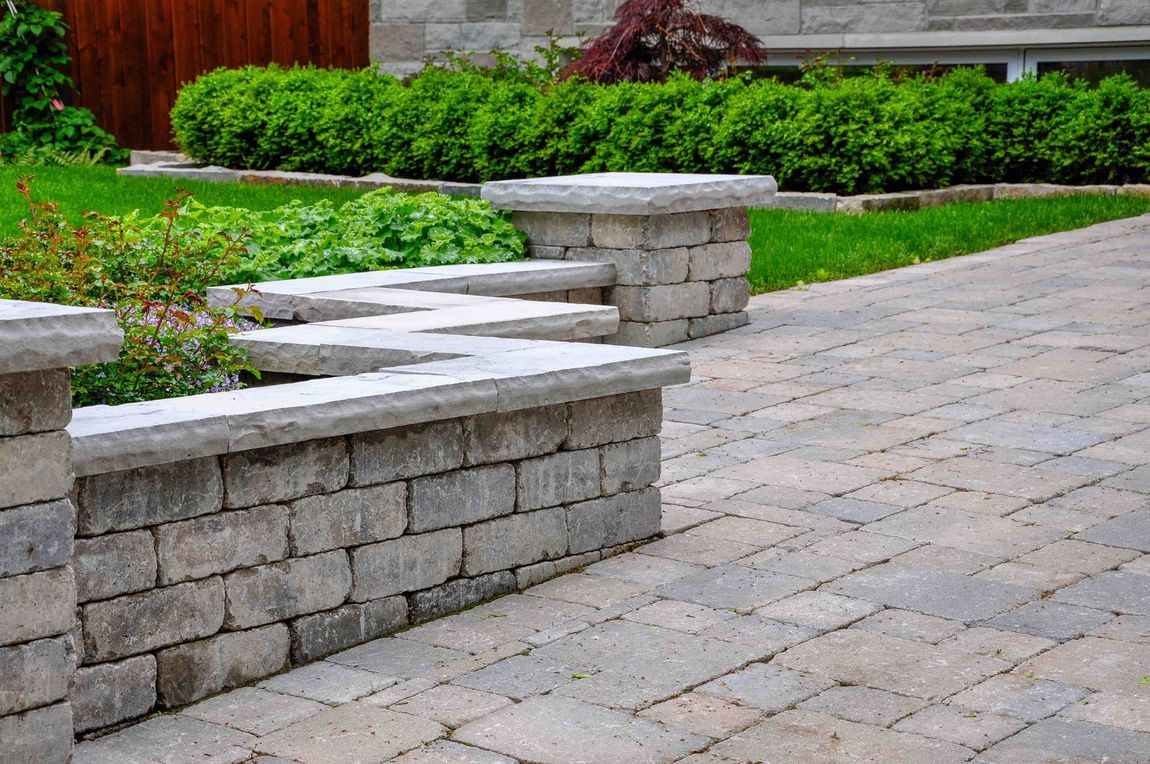 Stone paved pathway with retaining wall and garden, lush green bushes in background.