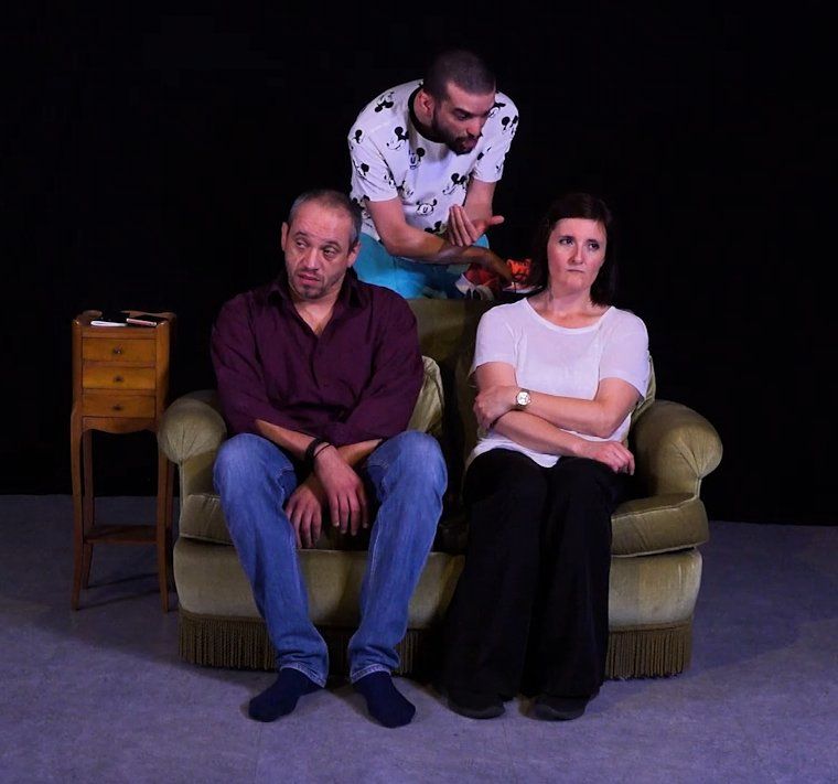Trois personnes assises sur un canapé, une quatrième debout derrière elles, dans un studio à l'éclairage tamisé.