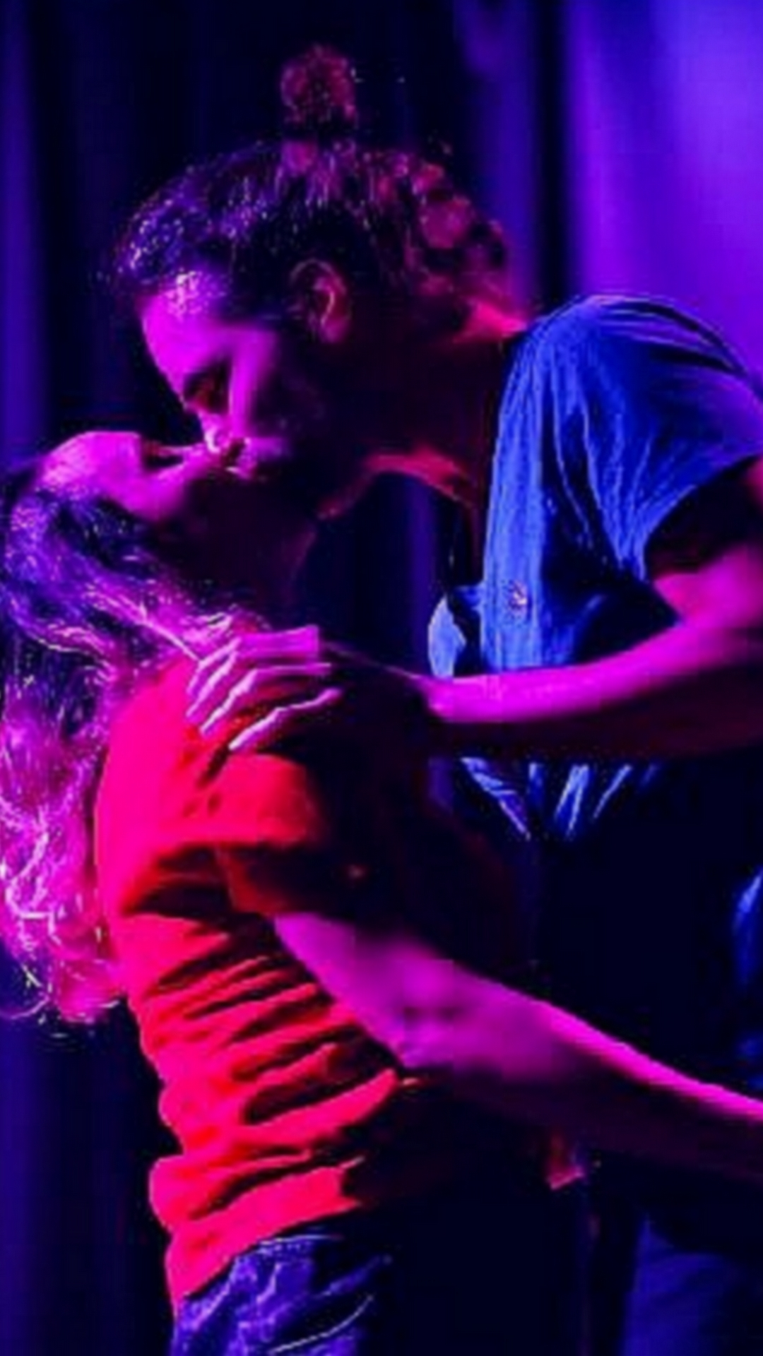 Deux personnes s'enlaçant sous les projecteurs violets de la scène, l'une se penchant pour embrasser le front de l'autre.