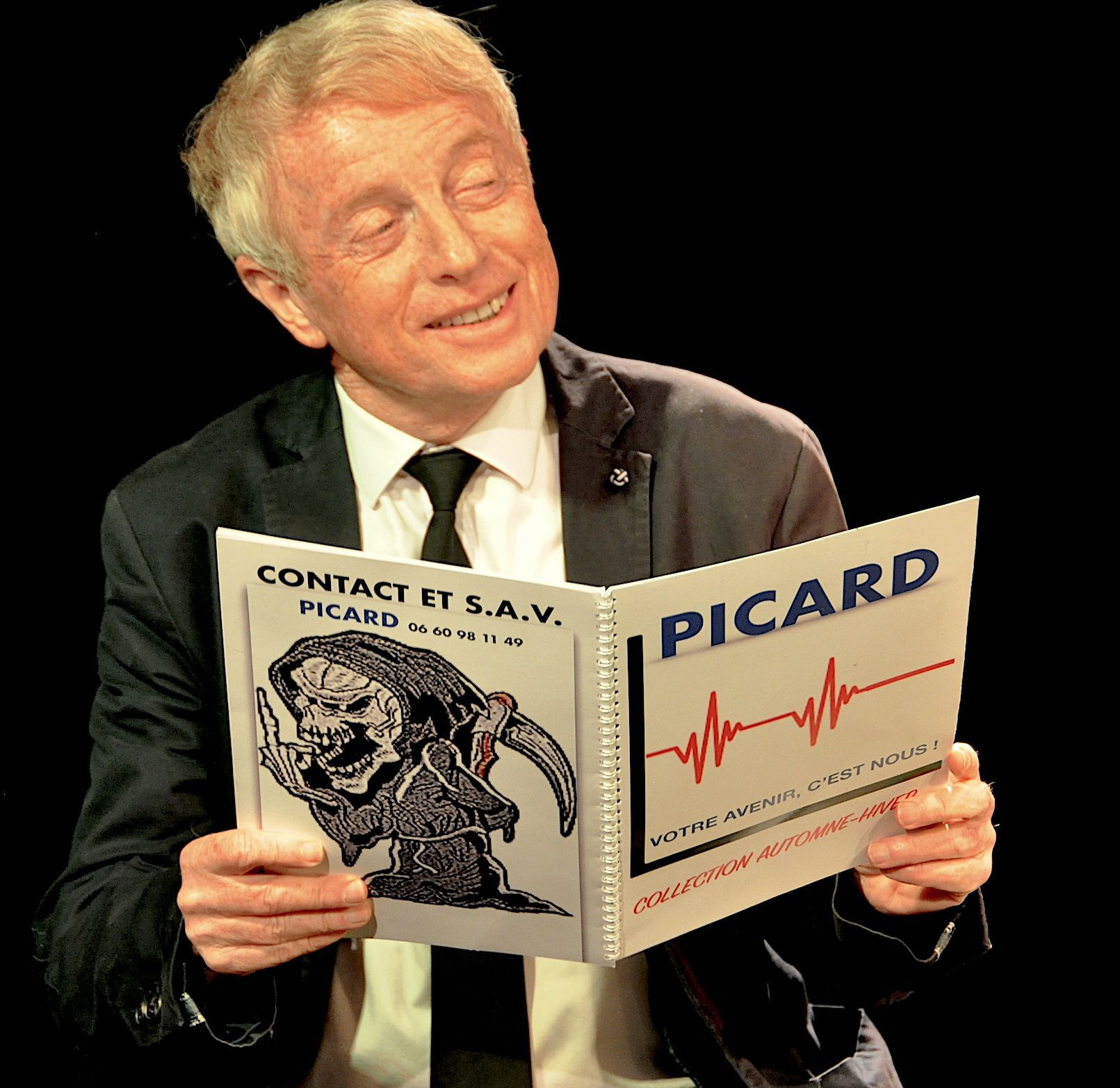 Un homme souriant en costume lit une brochure PICARD sur fond noir.