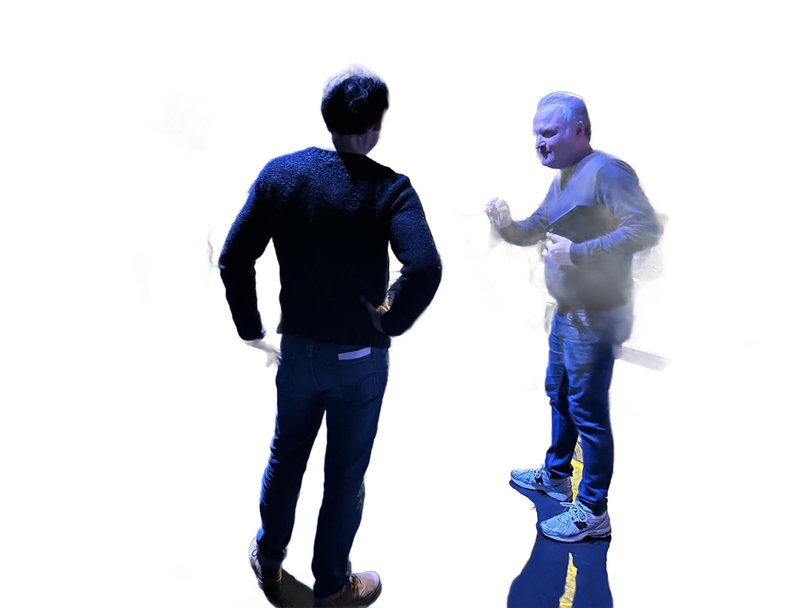 Deux personnes debout, discutant dans une pièce lumineuse, majoritairement blanche, l'une tournée vers l'extérieur et l'autre faisant des gestes.