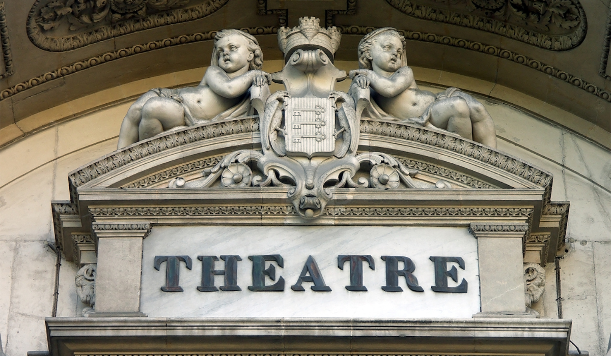 극장 건물의 석조 외관으로, 대문자로 "THEATRE"라는 글자가 새겨져 있고 그 위에는 조각상이 있다.
