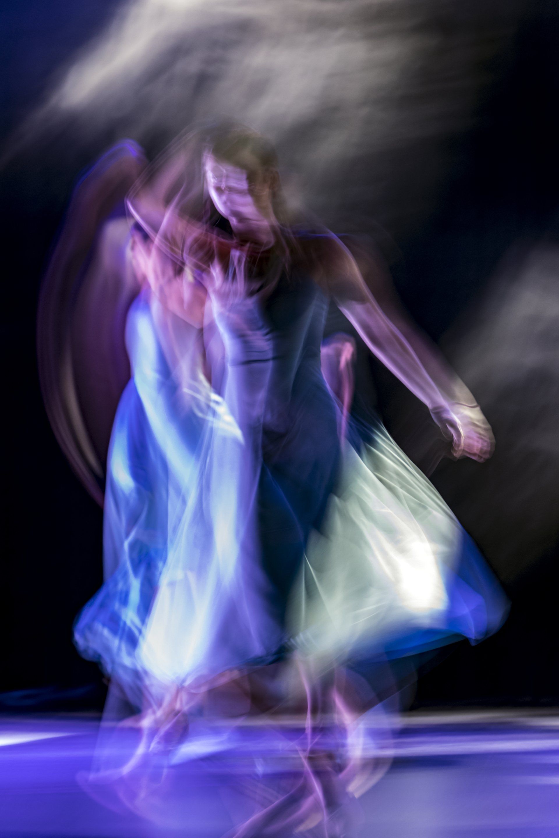 Danseuse floue en robe bleue fluide sous les projecteurs, saisie en mouvement sur fond sombre
