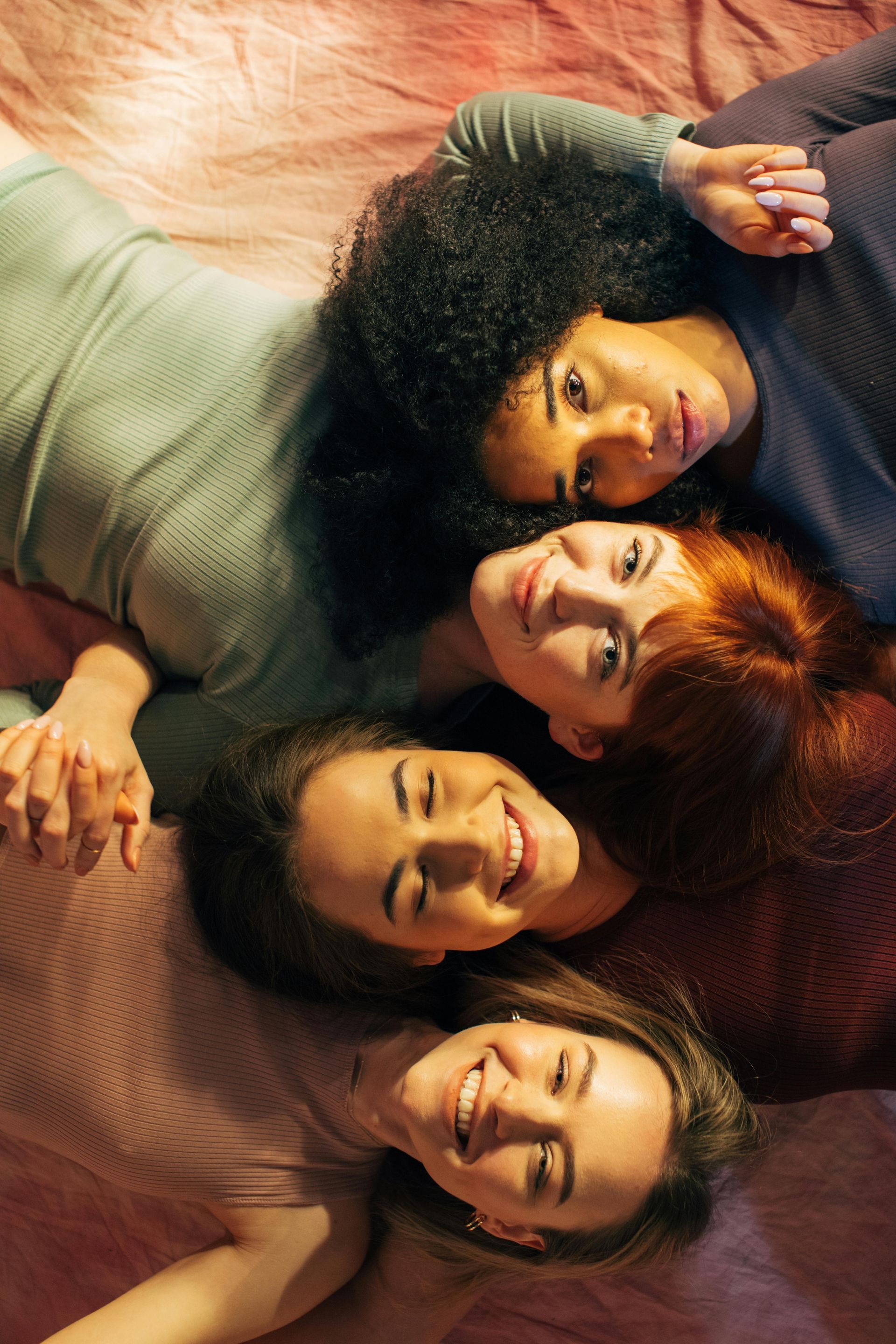 Quatre amis allongés côte à côte, souriant à l'objectif sur des couvertures colorées.