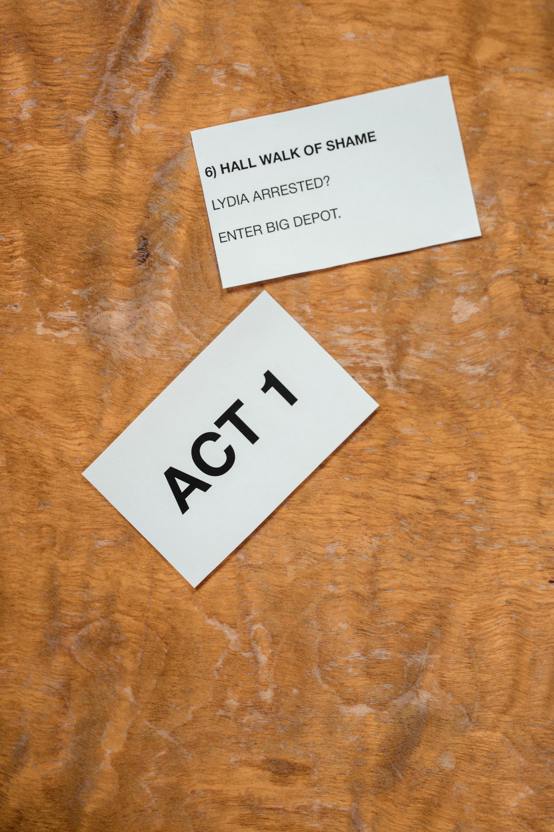 Deux cartes blanches posées sur une surface en bois, l'une portant l'inscription « ACTE 1 » et l'autre de petites notes manuscrites.